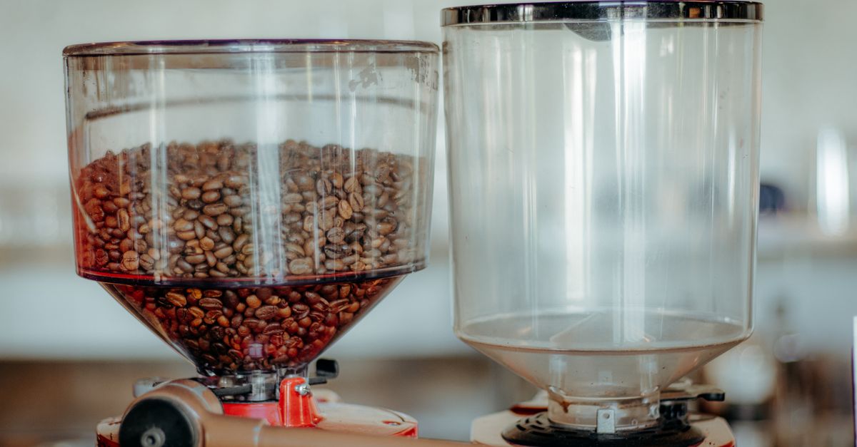 Close-up of a commercial coffee grinder with a full bean hopper in a cafe setting.